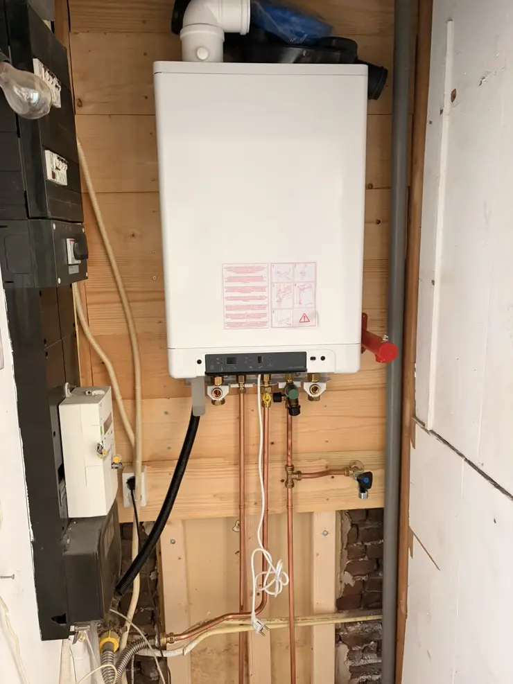 A new boiler fitted on a fresh mounting board in a meter cupboard