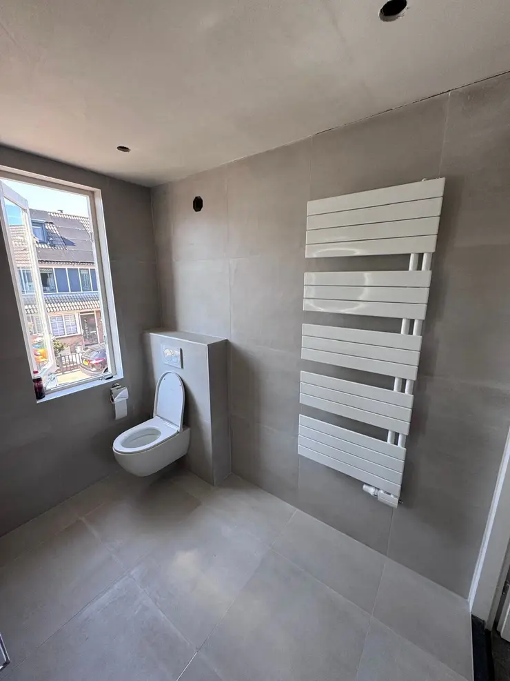 A tall white designer radiator on a newly tiled bathroom wall